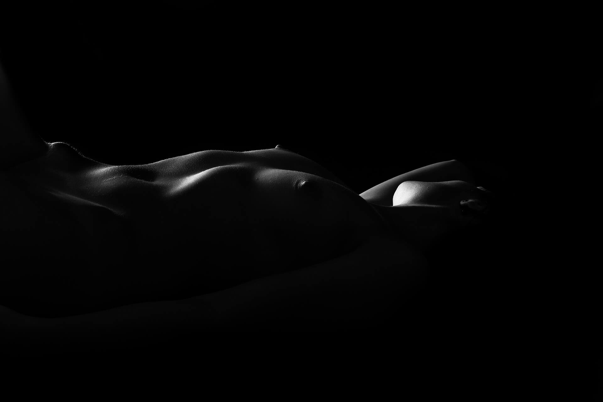 Tehnică Chiaroscuro aplicată în fotografia nude, detalii de lumină și umbră pe forme anatomice, portret artistic de studio low-key.