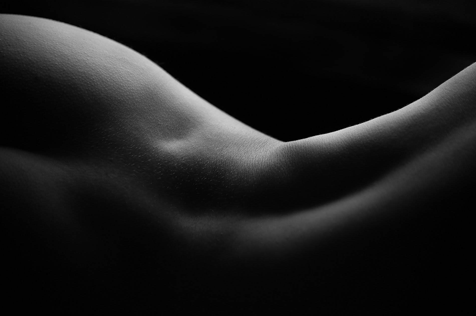 Studiu fotografic abstract alb-negru reprezentând curburile corpului uman ca un peisaj de dune, cu accent pe textura pielii și contrast fin.